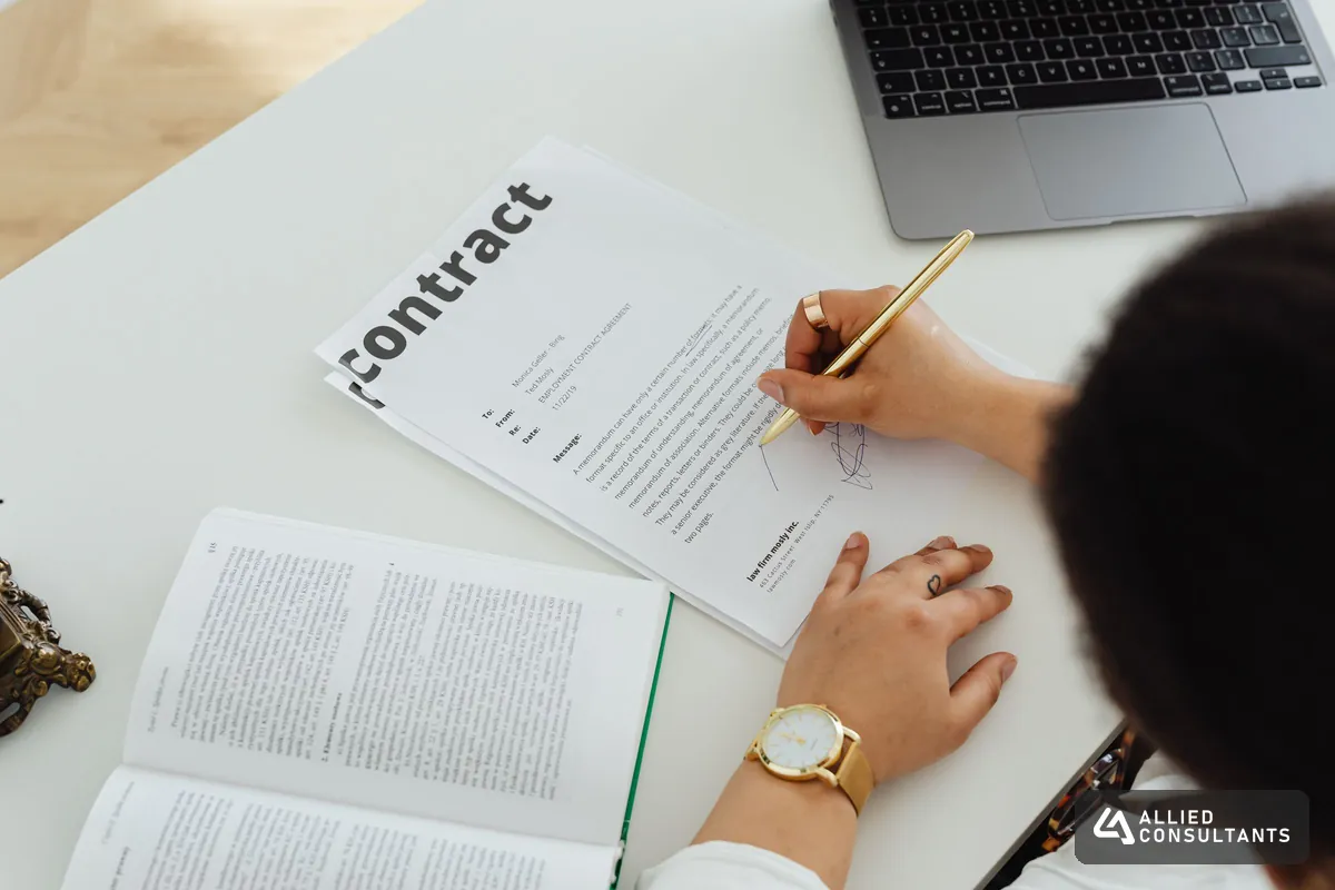Person reviewing and signing a contract next to a laptop