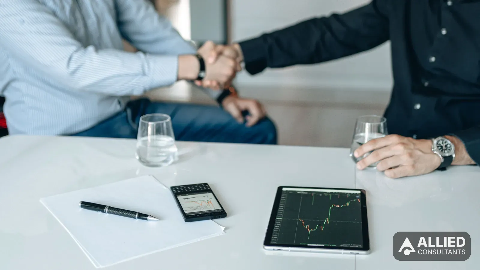 Seller and buyer shaking hands at a table with a tablet showing financial analysis of the business